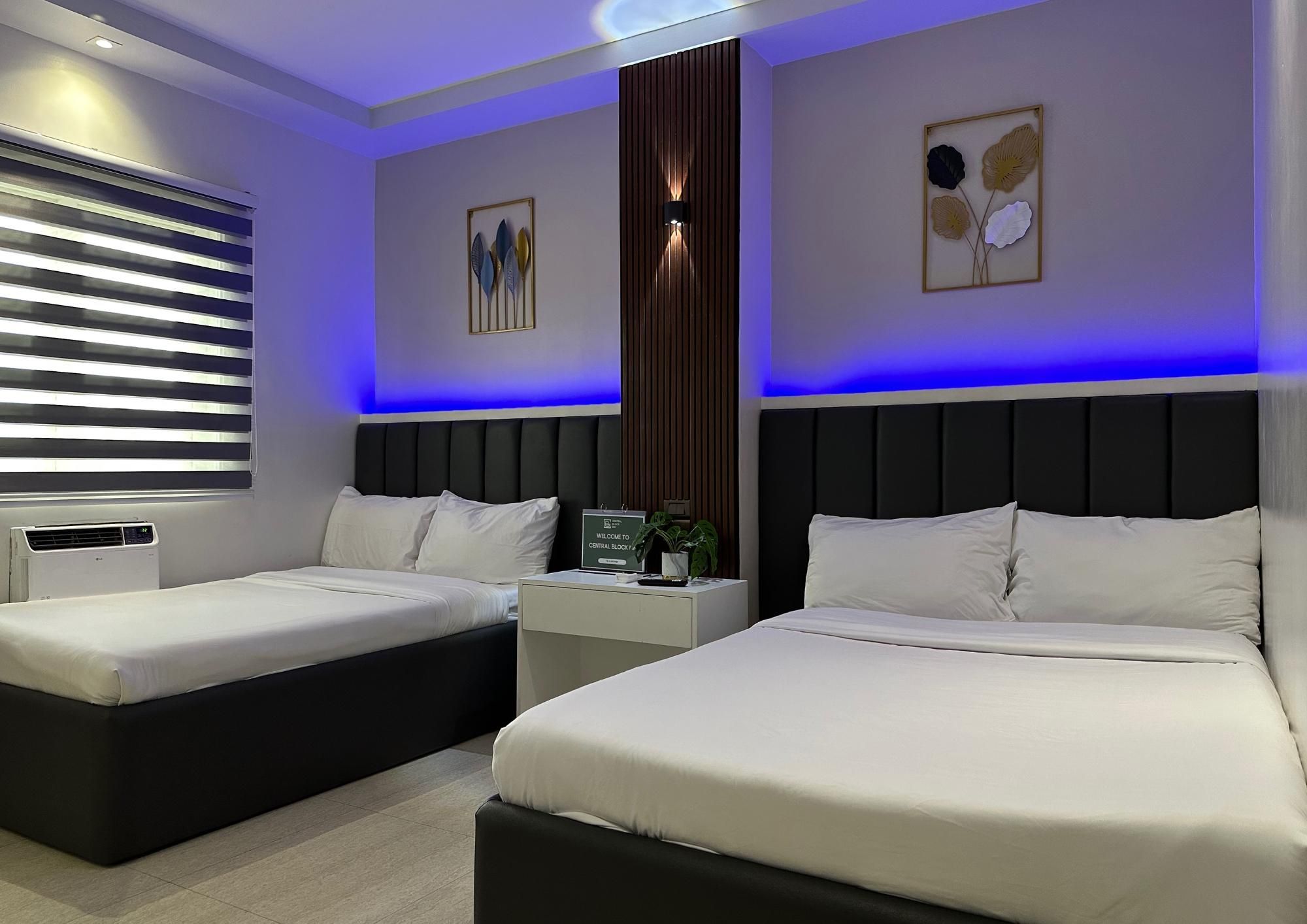 A modern hotel room with two beds, a nightstand, a wall-mounted air conditioner, and a window with blinds.