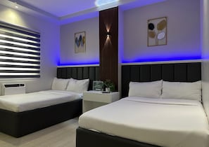 A modern bedroom with two beds, a nightstand, a wall-mounted lamp, and a window with blinds. - Central Block Inn (Bacolod)