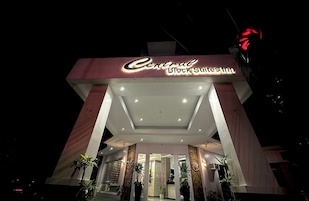 The exterior of Central Block Suites Inn with a prominent illuminated sign, a modern entrance with glass doors, and potted plants at the entrance.