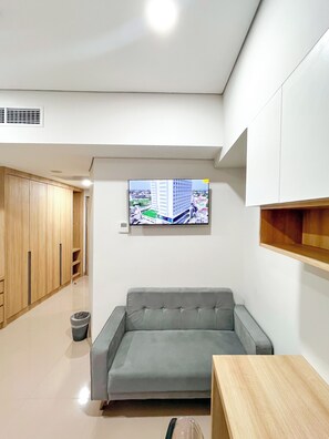 A modern living room with a grey sofa, wooden cabinets, a television mounted on the wall, and a small table. - University Hotel UMY (Depok)