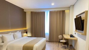 Habitación de hotel con una cama grande, un escritorio con silla, televisor y ventana con cortinas.