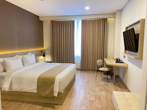A hotel room with a large bed, a desk with a chair, a television, and a window with curtains. - University Hotel UMY (Depok)