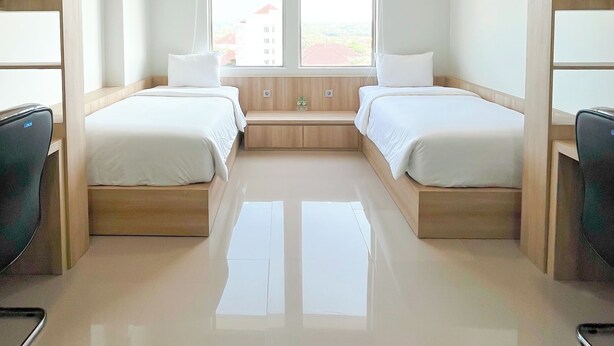 Habitación de hotel con dos camas, un pequeño banco, un escritorio y vistas a edificios.