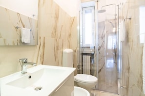Um banheiro moderno com pia de mármore, vaso sanitário e chuveiro com box de vidro.