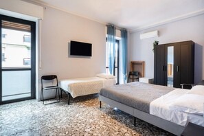 Quarto de hotel com cama, cadeira, televisão, guarda-roupa e janela com cortinas.