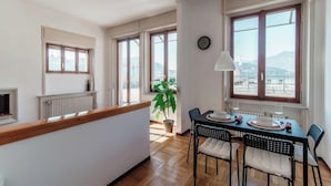 A dining area with a table set for two, a potted plant, and a view of the outdoors through large windows. - Terrazza Rooftop (Como)