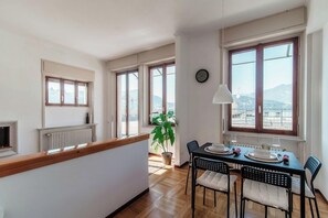 Un coin repas avec une table dressée pour deux personnes, une plante en pot et une vue sur l’extérieur grâce à de grandes fenêtres.