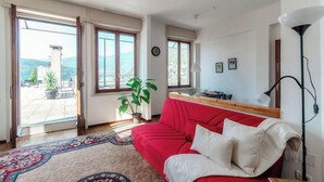 A room with a red sofa, a patterned rug, a potted plant, and a view through large windows. - Terrazza Rooftop (Como)