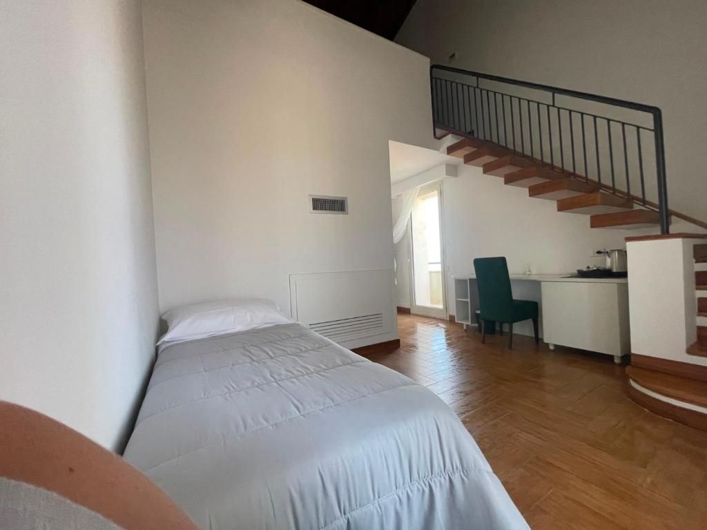 A bedroom with a bed, a desk, and a chair. There is a staircase with a railing.