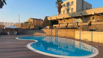 A swimming pool with a stone wall and a building with a balcony.