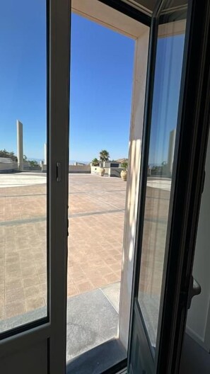 A view through a glass door to an outdoor patio area with a tiled floor and a clear sky. - KENTO RESORT (Centuripe)
