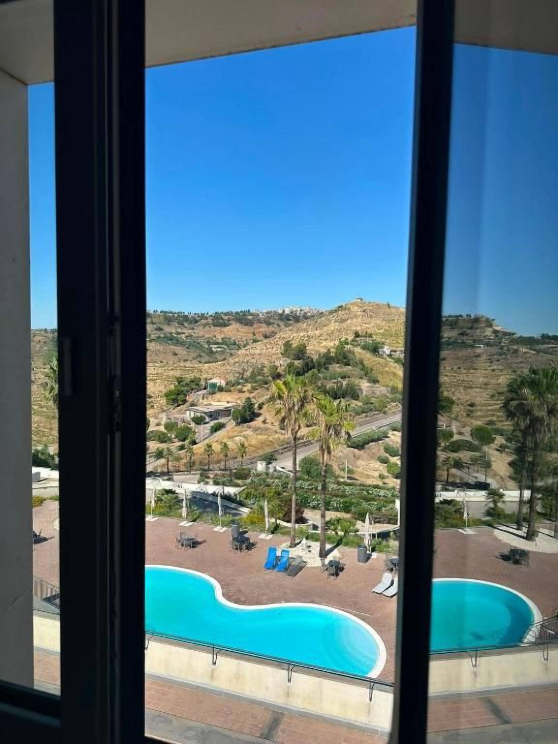 Blick aus einem Fenster auf einen Swimmingpool und eine hügelige Landschaft.