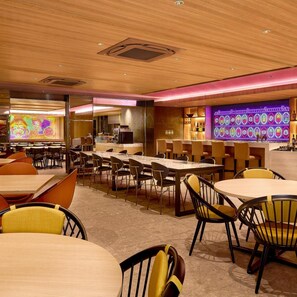 Un restaurant doté de nombreuses tables et chaises, d'un bar avec des enseignes lumineuses au néon et d'une fresque colorée sur le mur.