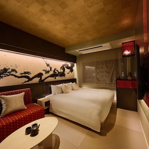 Une chambre d’hôtel avec un grand lit, un canapé rouge, une petite table avec deux tasses et un mur orné d’une œuvre d’art traditionnelle.