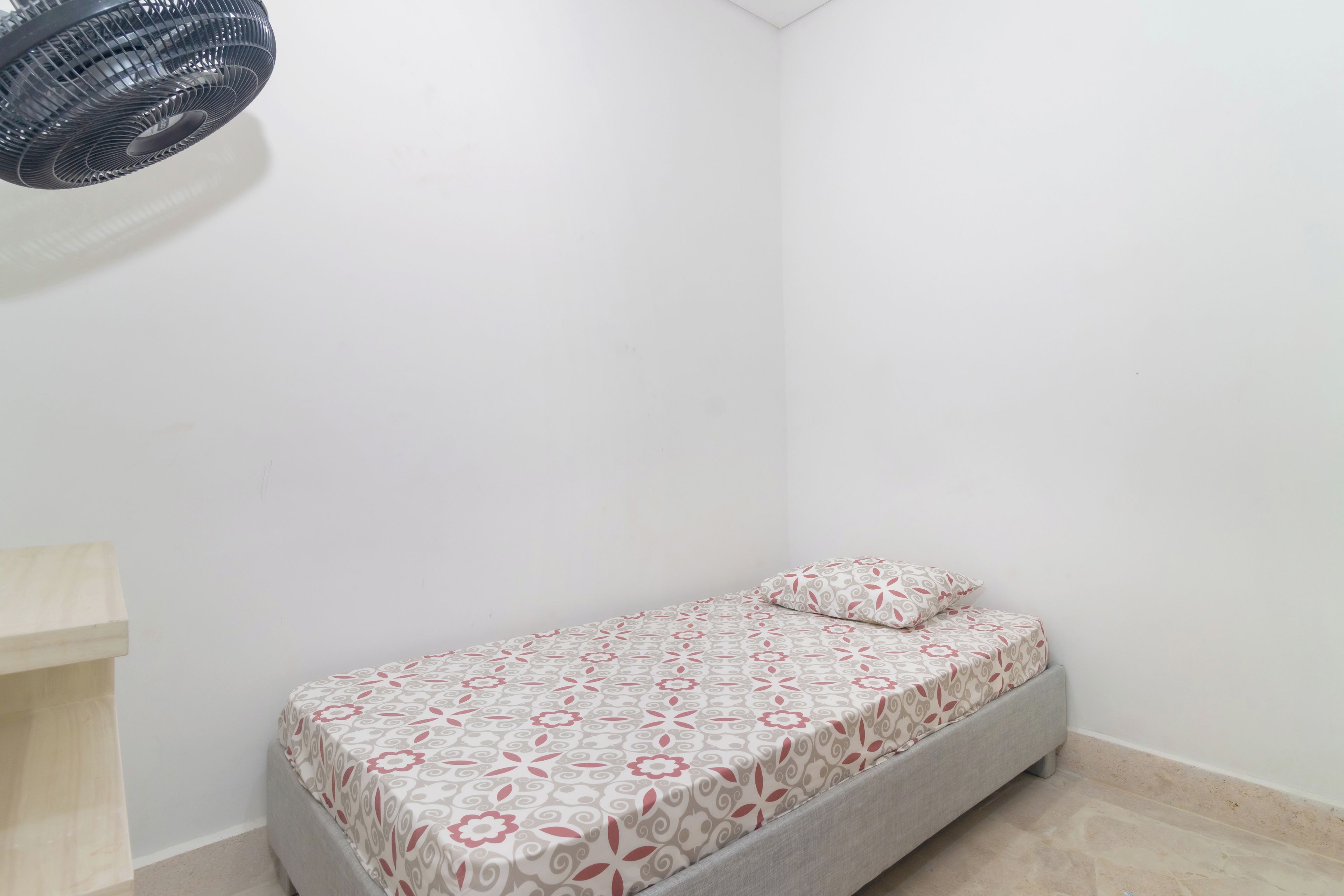 Ein kleines Zimmer mit einem Einzelbett, einer gemusterten Bettdecke und einem Kopfkissen.