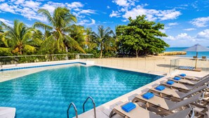 Une piscine d’un bleu éclatant, avec des chaises longues et un palmier en arrière-plan.