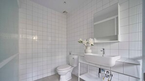 A modern bathroom with white tiles, a toilet, a sink, and a mirror. - M Village Living Dien Bien Phu (Ho Chi Minh Municipality)