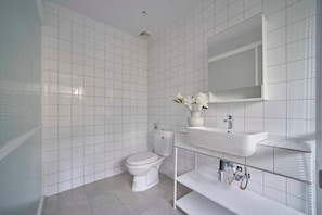A modern bathroom with white tiles, a toilet, a sink, and a mirror. - M Village Living Dien Bien Phu (Ho Chi Minh Municipality)