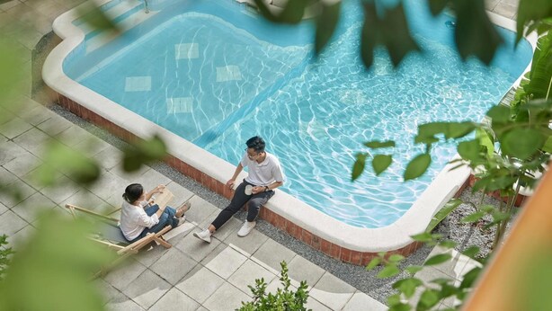 An outdoor swimming pool with a curved edge, surrounded by a tiled deck and a brick border. - M Village Living Dien Bien Phu (Ho Chi Minh Municipality)