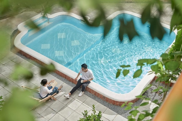 An outdoor swimming pool with a curved edge, surrounded by a tiled deck and a brick border. - M Village Living Dien Bien Phu (Ho Chi Minh Municipality)