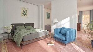 A modern bedroom with a bed, a blue armchair, a small table with a vase of flowers, and a floor lamp. - M Village Living Dien Bien Phu (Ho Chi Minh Municipality)