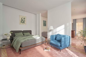 A modern bedroom with a bed, a blue armchair, a small table with a vase of flowers, and a floor lamp. - M Village Living Dien Bien Phu (Ho Chi Minh Municipality)