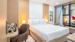 Ein Hotelzimmer mit einem Bett, zwei Nachttischlampen, einem Sessel, einem Schreibtisch, einem Spiegel und einem Deckenventilator.