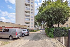 Eine Wohnstraße mit parkenden Autos, einem hohen Wohnhaus und einem großen Baum.
