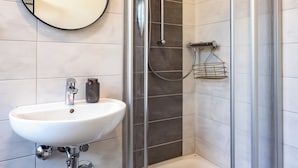 Een moderne badkamer met een douchecabine van glas, een ronde spiegel en een wit wastafelmeubel.