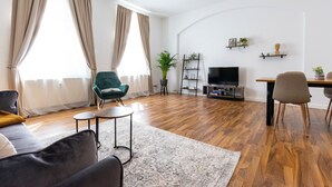 Een moderne woonkamer met een bank, een groene fauteuil, een salontafel, een televisie en een eethoek met stoelen.