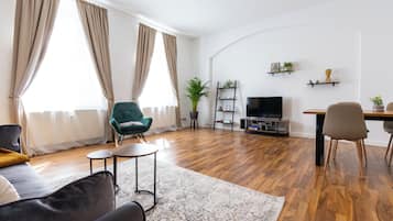 Ein modernes Wohnzimmer mit einer Couch, einem grünen Sessel, einem Couchtisch, einem Fernseher und einem Essbereich mit Stühlen.