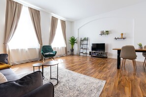 En moderne stue med sofa, lænestol i grøn, sofabord, fjernsyn og spiseplads med stole.