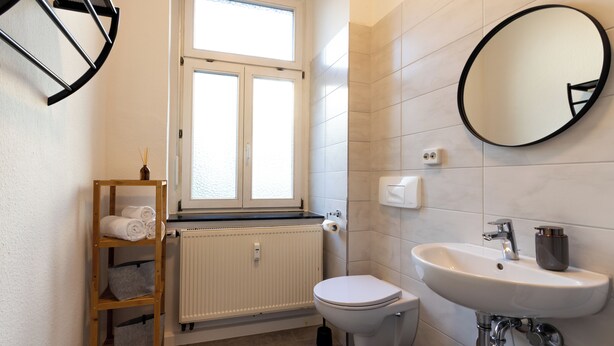 Een badkamer met toilet, wastafel, spiegel, raam en handdoekhouder.