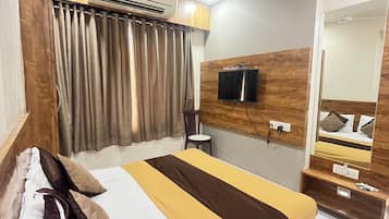 Habitación de hotel con cama, cortinas, aire acondicionado, ventilador de techo, televisor y espejo.