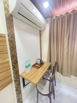 A room with a wooden table, two chairs, an air conditioning unit, a curtain, and a tiled wall with a patterned section.