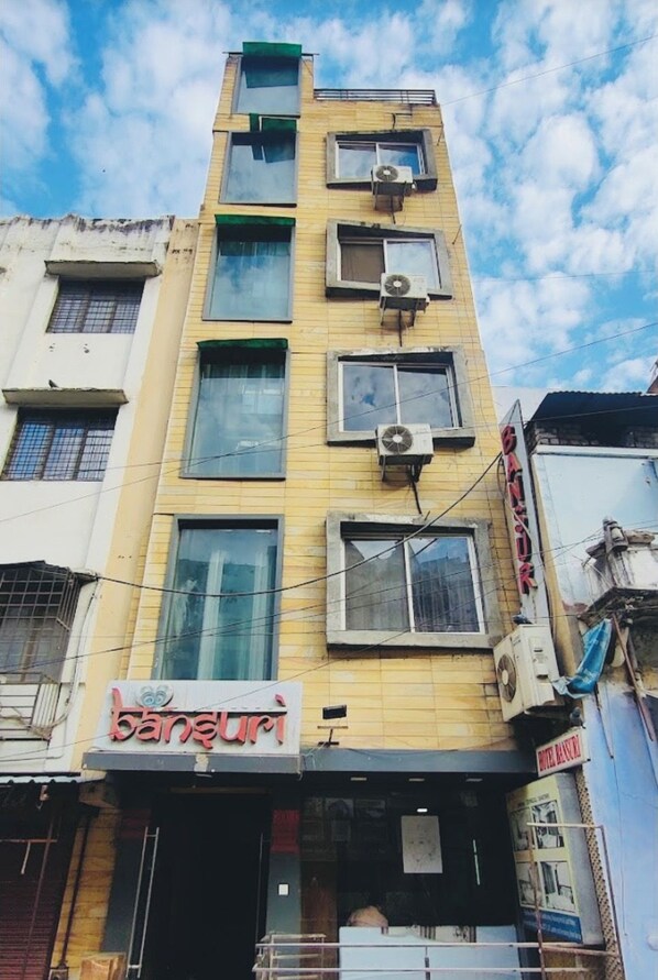 A multi-story building with air conditioning units, a visible storefront with signage, and a clear sky.