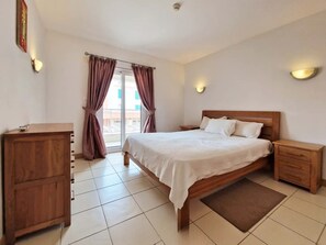 A bedroom with a bed, nightstands, a wooden dresser, and a view through the window. - Sunny 1-Bedroom Apartment Island Retreat with Pool Views at Vila Verde Resort (Sal)