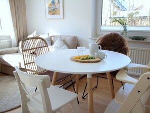 A dining area with a round table, white chairs, a white pitcher, a glass, and a plate of fruit. - Holiday Apartment With 2 Bedrooms (Zingst)