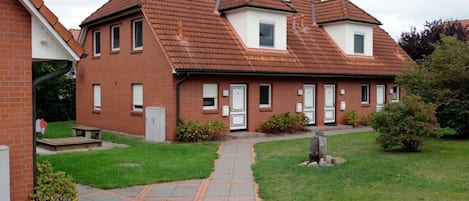 A two-story brick house with a tiled roof, a paved pathway leading to the entrance, and a small garden area.