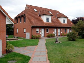 A two-story brick house with a tiled roof, a paved pathway leading to the entrance, and a small garden area. - Holiday Apartment With 2 Bedrooms (Zingst)