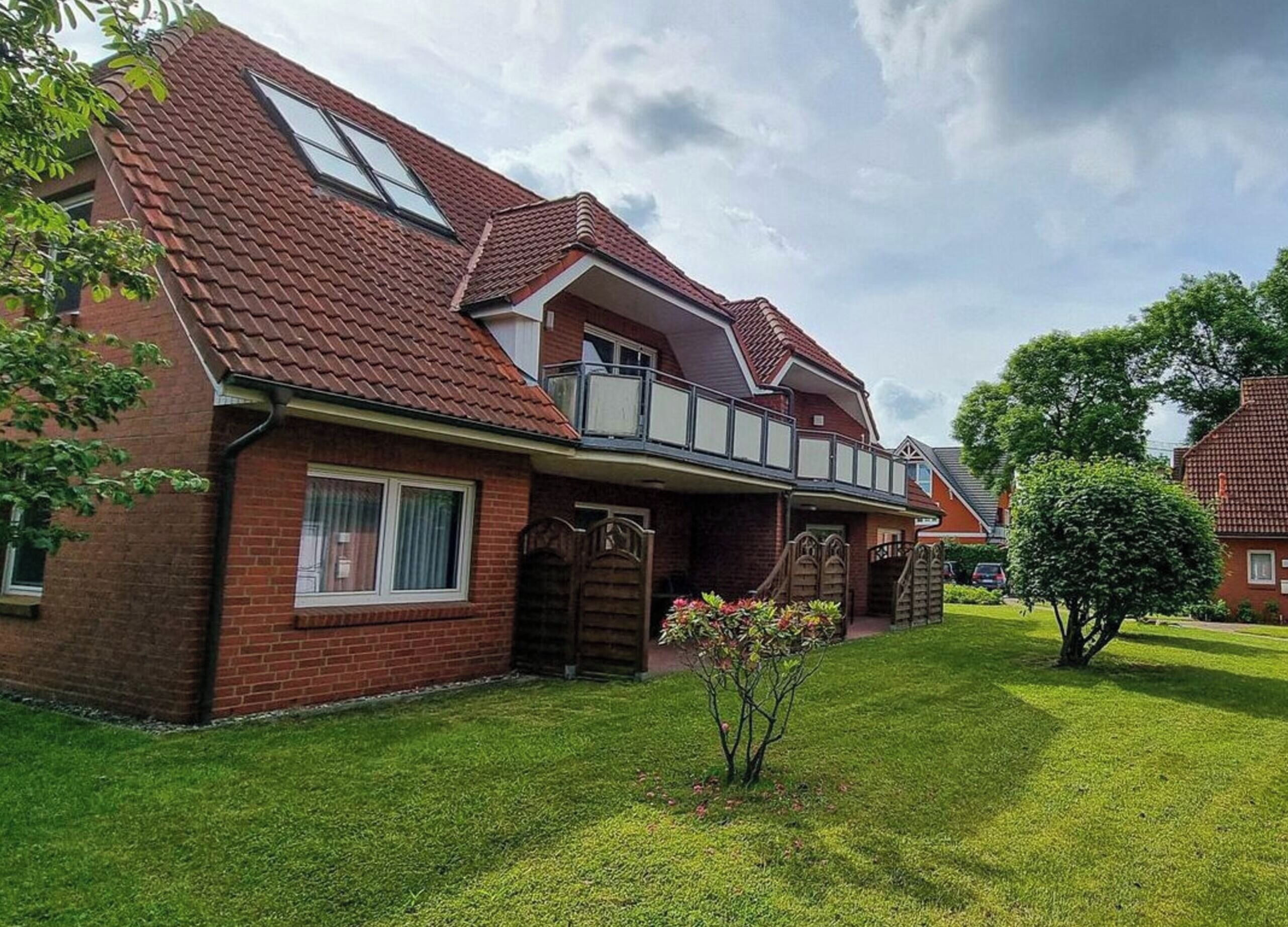 Une maison à deux étages avec une façade en briques rouges, un balcon et une pelouse bien entretenue.