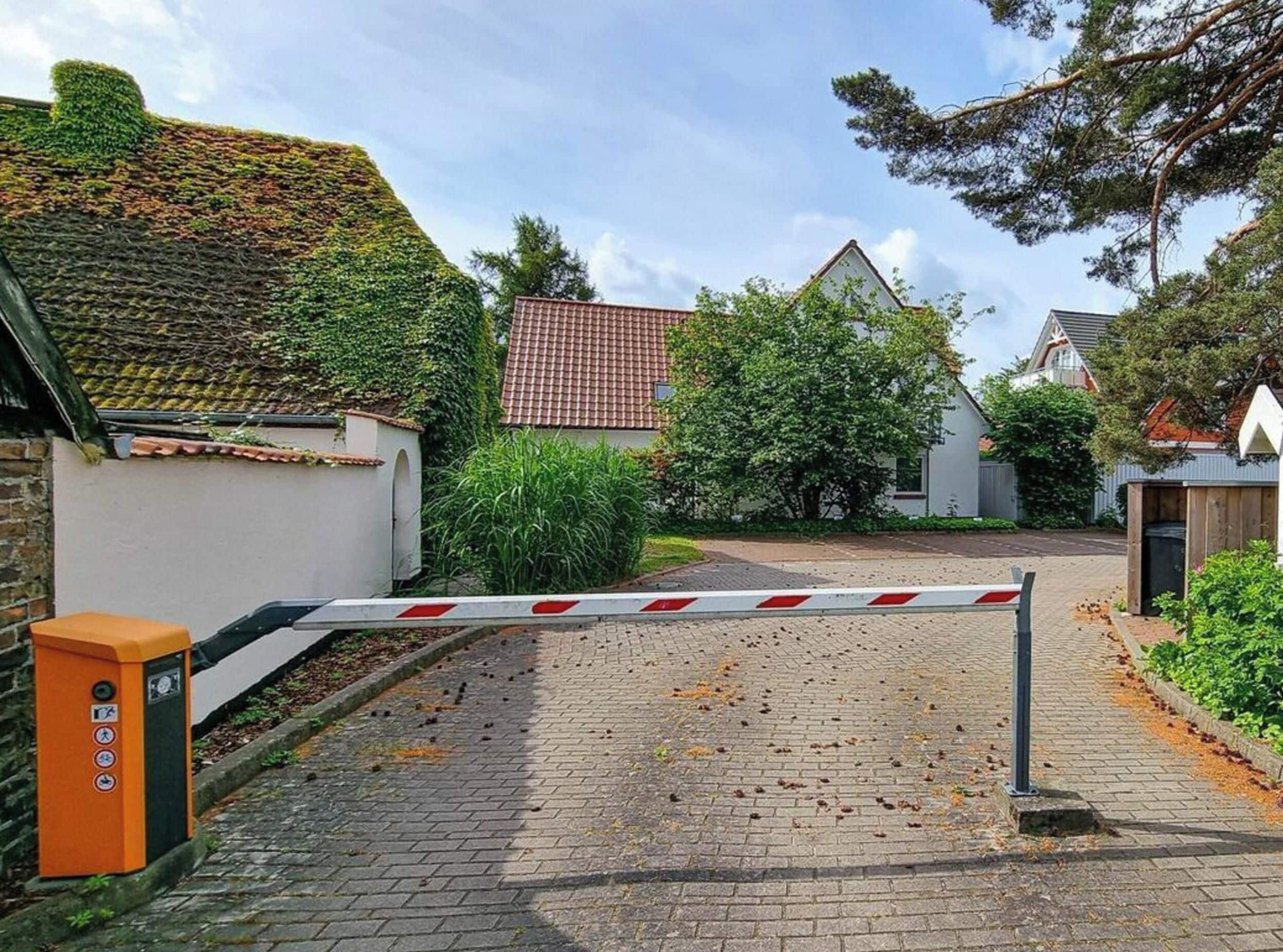 En lukket indgang med en rød og hvid bom, en murstenssti og en lille orange el-tavle.