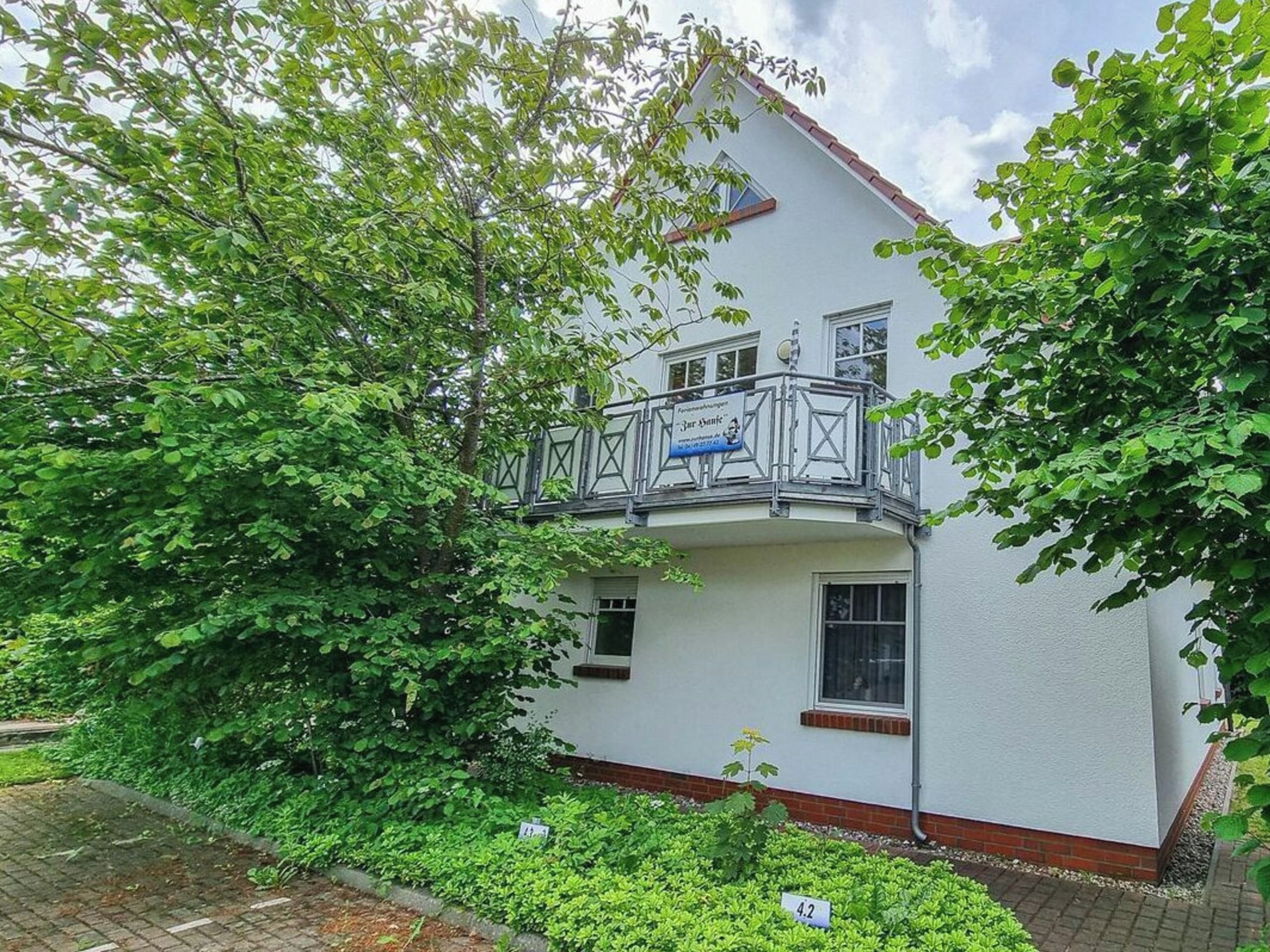 Ein zweistöckiges Gebäude mit Balkon, umgeben von üppiger Vegetation.