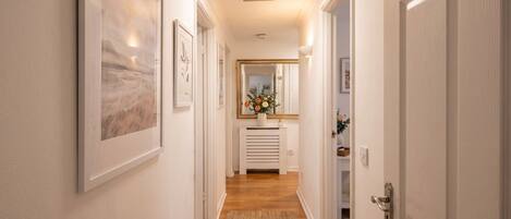 A hallway with framed artwork on the walls, a white radiator, and a door on the right.