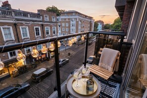 A balcony with a view of a street, a table with drinks, and a chair. - 2-Bed Flat Sleeps 6 · Balcony · Walk to Earl`s Court Tube (Greater London)