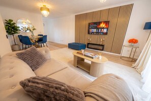 A modern living room with a sofa, coffee table, and a flat-screen TV mounted on a wooden wall. - 2-Bed Flat Sleeps 6 · Balcony · Walk to Earl`s Court Tube (Greater London)