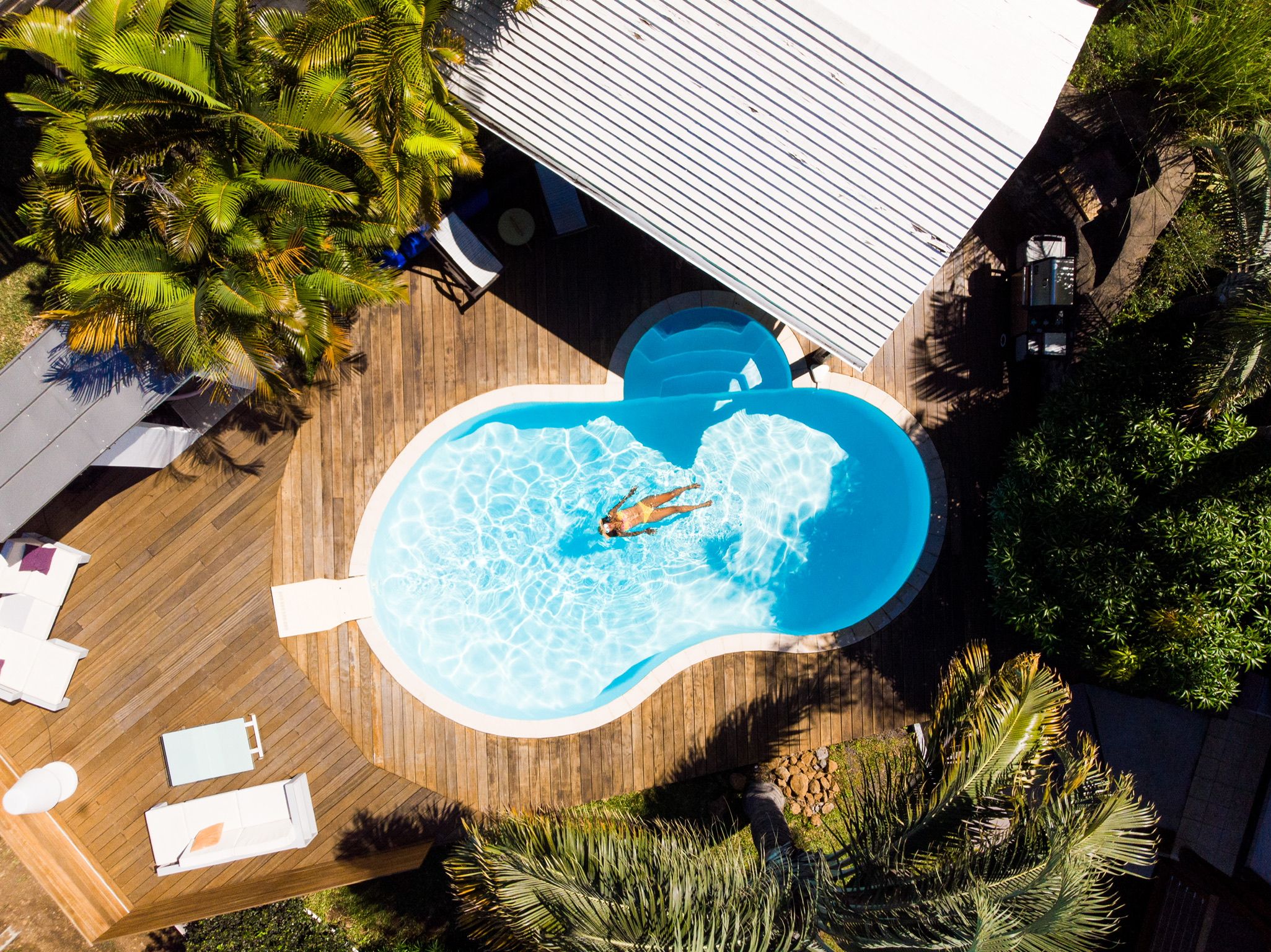 Eine Vogelperspektive auf einen Swimmingpool, umgeben von Holzterrassen und Palmen.