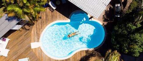 An aerial view of a swimming pool surrounded by wooden decking and palm trees.