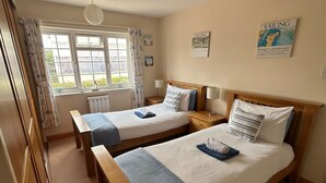 A hotel room with two single beds, a window with curtains, a radiator, and a wall-mounted map. - Guernsey 2 bedroom cottage near Perelle Bay (Saint Saviour)