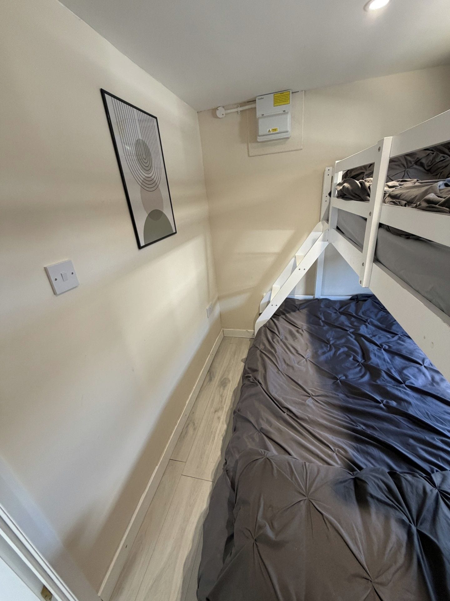 Ein kleiner, kompakter Raum mit Etagenbett, einem Einzelbett, einer fest installierten Klimaanlage und einem gerahmten Bild.